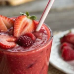 Vaso alto con smoothie de frutos rojos cremoso, decorado con fresas, arándanos y frambuesas frescas.